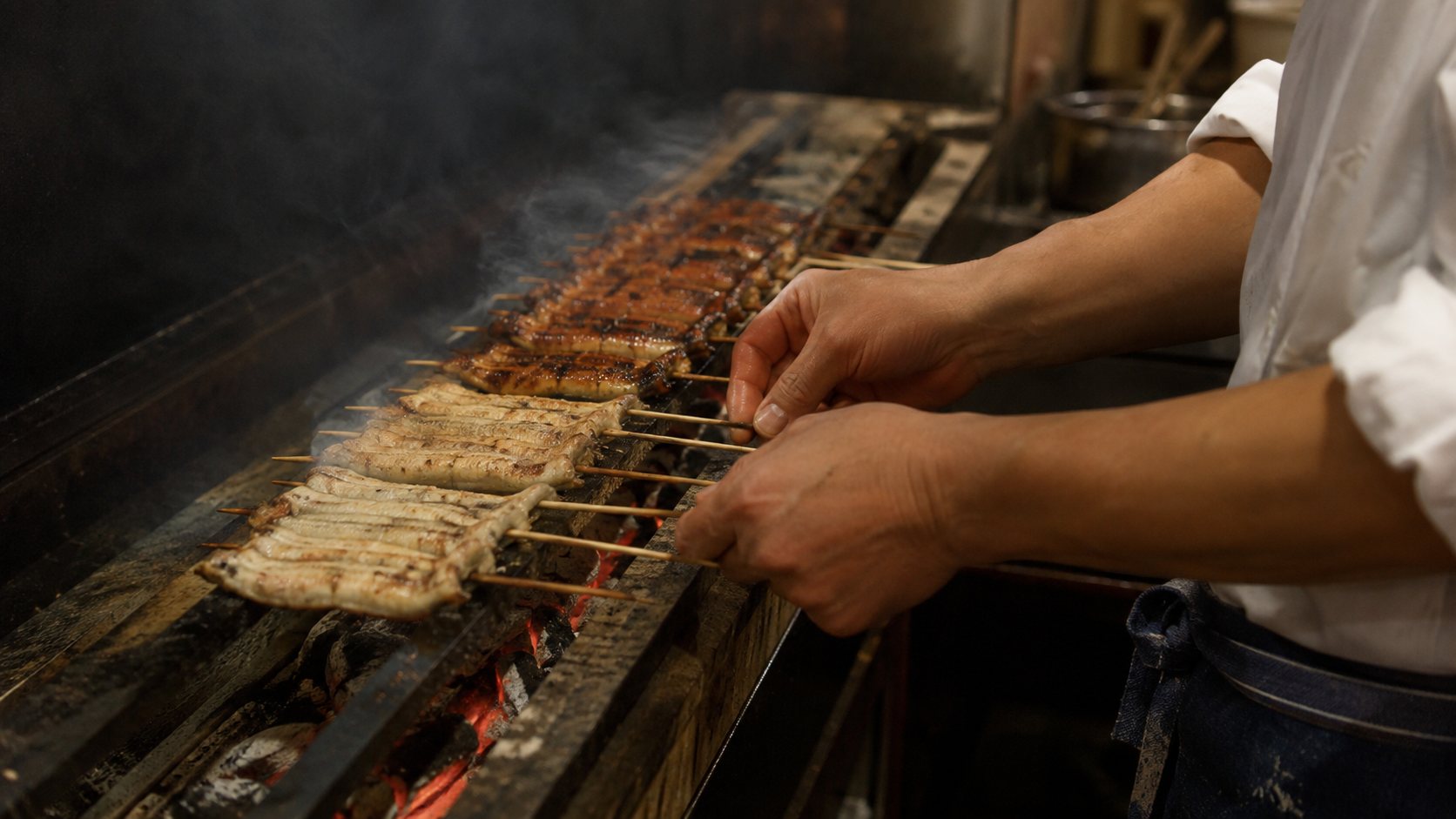 炭床の上で竹串を打った鰻を返す焼き場の手元